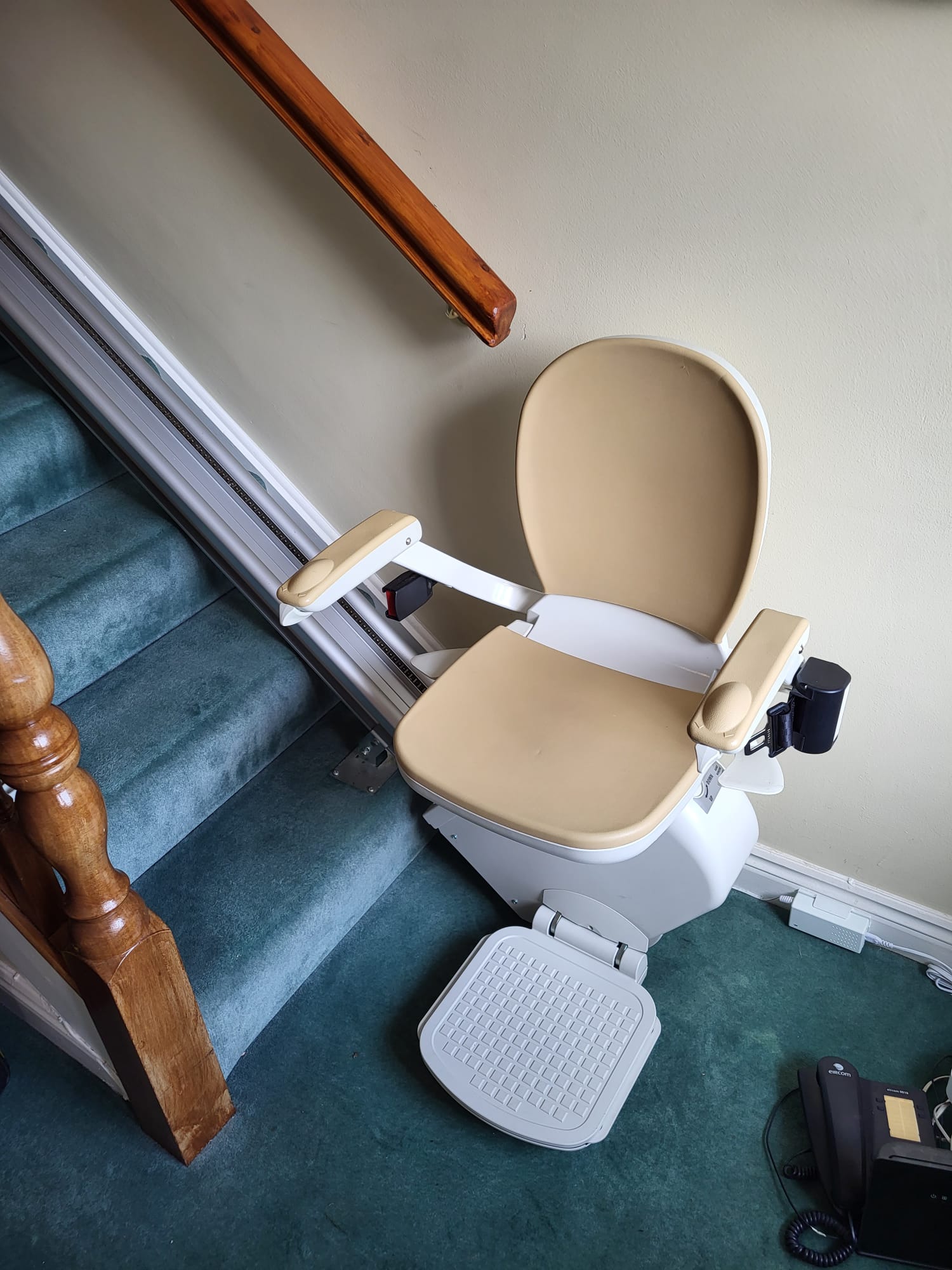 Cream covered stairlift with white base and frame. On a blue carpet covered staircase with cream walls